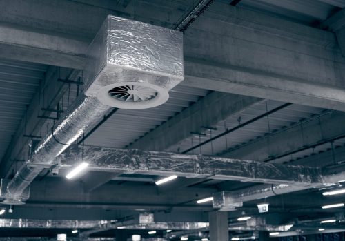 Air ventilation system on the ceiling in a large warehouse. Pipes made of silver insulating material hang from the ceiling inside the new building